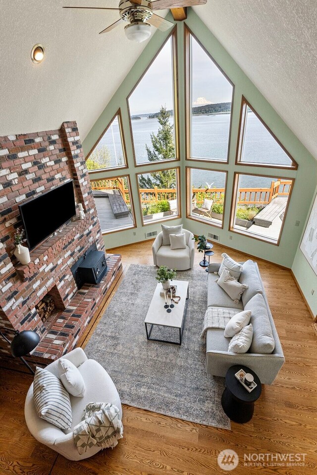 living area featuring a water view, a textured ceiling, a ceiling fan, wood finished floors, and high vaulted ceiling