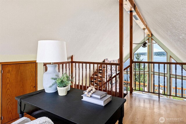 office area with ceiling fan, a water view, wood finished floors, a textured wall, and a textured ceiling