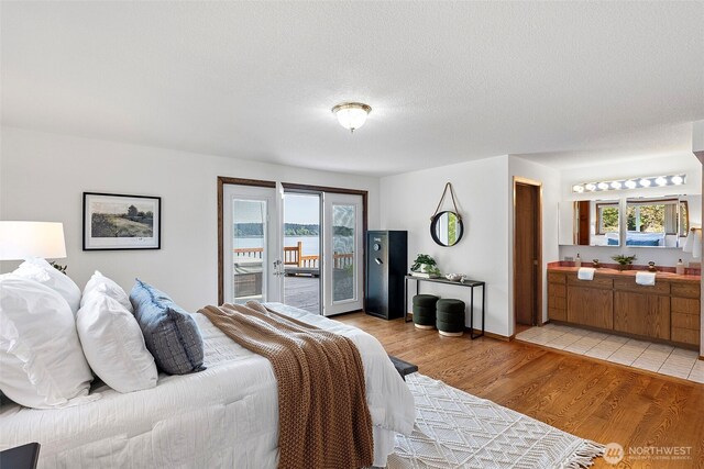 bedroom with access to outside, ensuite bathroom, and light wood-type flooring