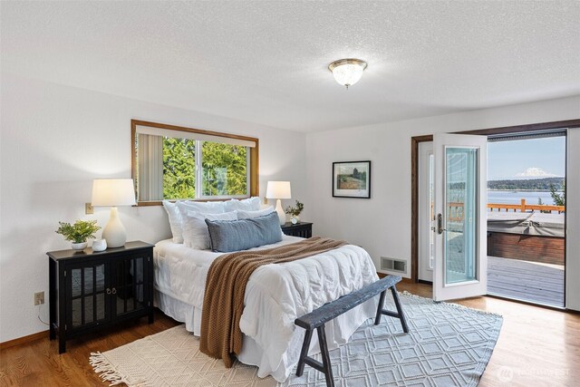 bedroom with access to outside, wood finished floors, a textured ceiling, and baseboards