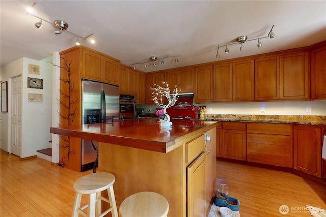 18 Blue Creek Rd, Walla Walla, WA 99362 - kitchen featuring stainless steel appliances, light wood-style flooring, brown cabinetry, a breakfast bar area, and a center island