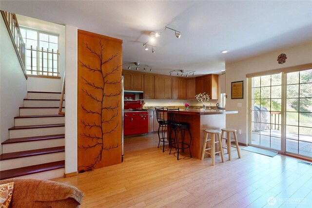 18 Blue Creek Rd, Walla Walla, WA 99362 - kitchen with a kitchen breakfast bar, light wood finished floors, a peninsula, brown cabinetry, and under cabinet range hood