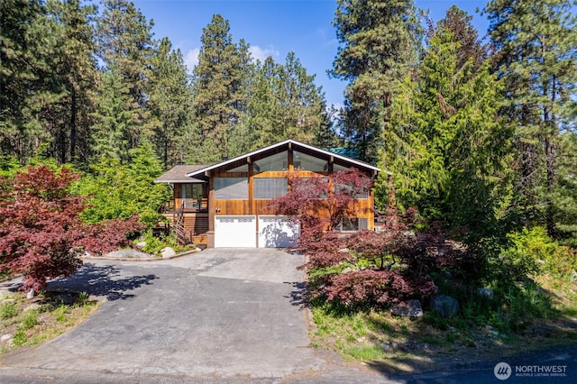 view of front of home featuring driveway, stairway, a garage, and a forest view