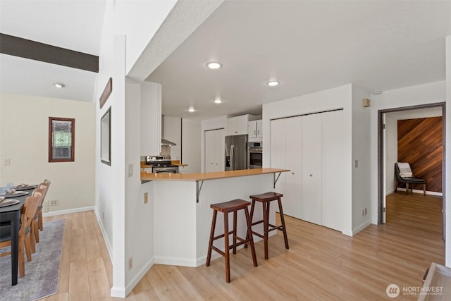 kitchen featuring stainless steel appliances, a peninsula, light wood finished floors, a breakfast bar area, and white cabinetry