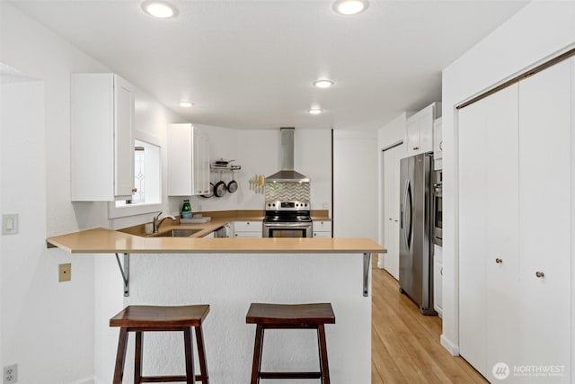 kitchen with appliances with stainless steel finishes, wall chimney range hood, a sink, a peninsula, and recessed lighting