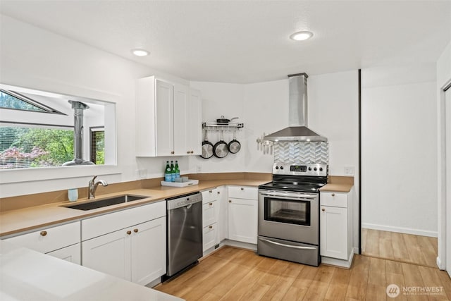 kitchen with stainless steel appliances, wall chimney range hood, a sink, white cabinets, and recessed lighting