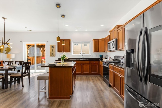 kitchen featuring stainless steel appliances, dark countertops, brown cabinetry, a center island, and a breakfast bar area
