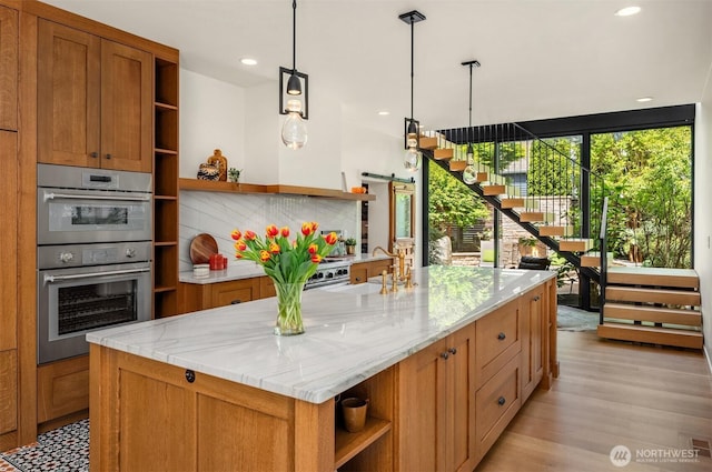 kitchen featuring open shelves, stainless steel double oven, a sink, brown cabinets, and a center island with sink