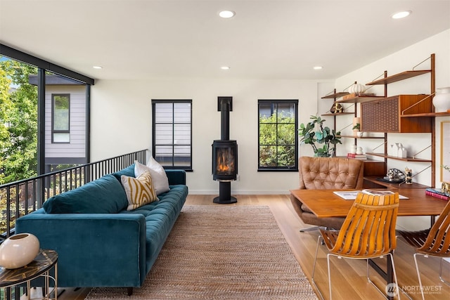 living room with wood finished floors, plenty of natural light, recessed lighting, a wood stove, and baseboards