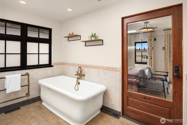full bath featuring tile walls, a freestanding tub, a wainscoted wall, and recessed lighting