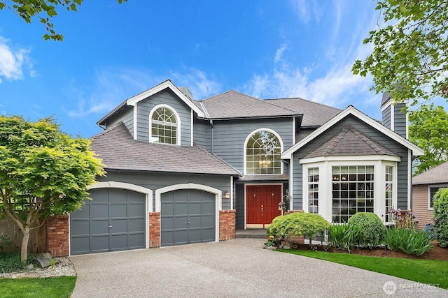 traditional-style house with driveway, a chimney, roof with shingles, brick siding, and an attached garage