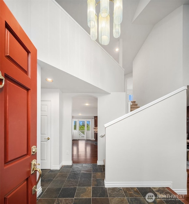 foyer entrance with a high ceiling, stone tile flooring, baseboards, recessed lighting, and a chandelier