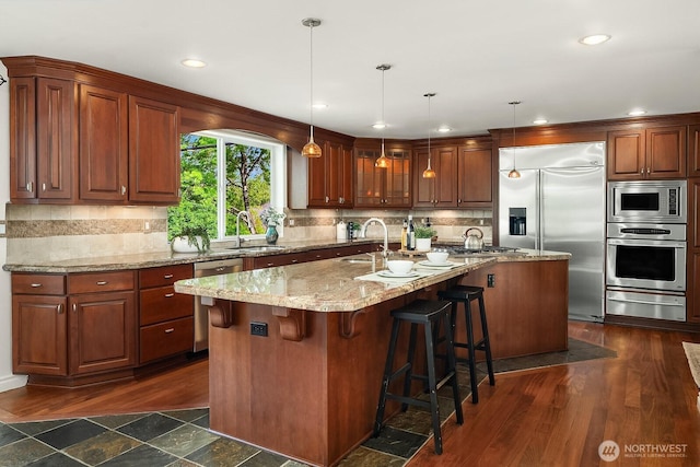 kitchen featuring built in appliances, a warming drawer, a sink, dark wood-style floors, and a center island with sink