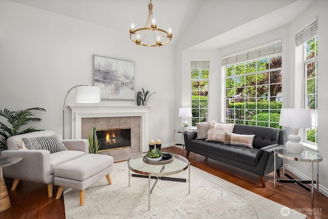 living area with wood finished floors, a chandelier, baseboards, vaulted ceiling, and a tiled fireplace