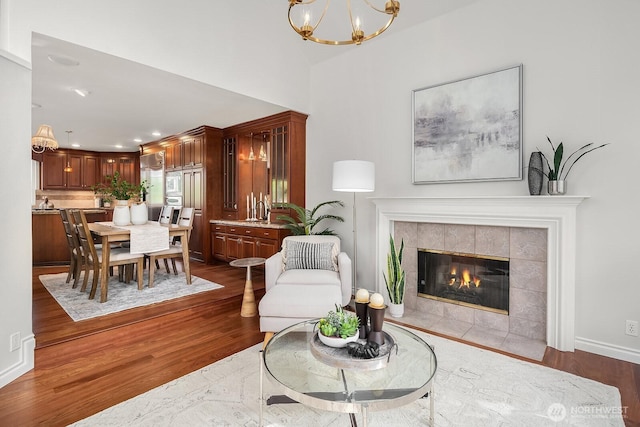 living area featuring dark wood-type flooring, a chandelier, a tiled fireplace, recessed lighting, and baseboards