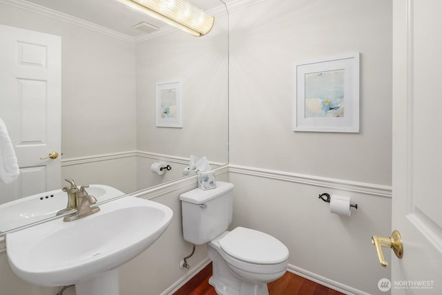 half bathroom with a sink, toilet, wood finished floors, ornamental molding, and baseboards