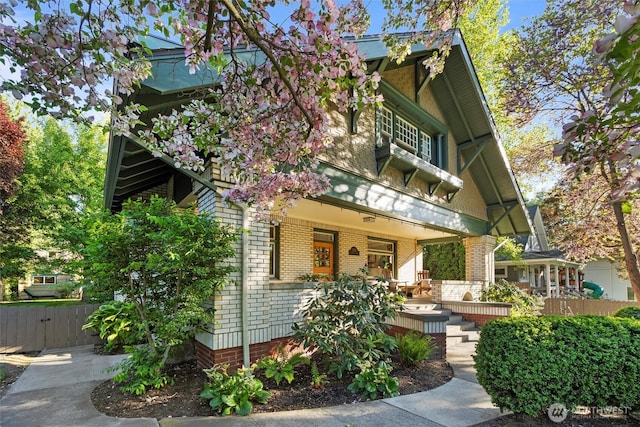 view of front facade featuring brick siding, a porch, and fence