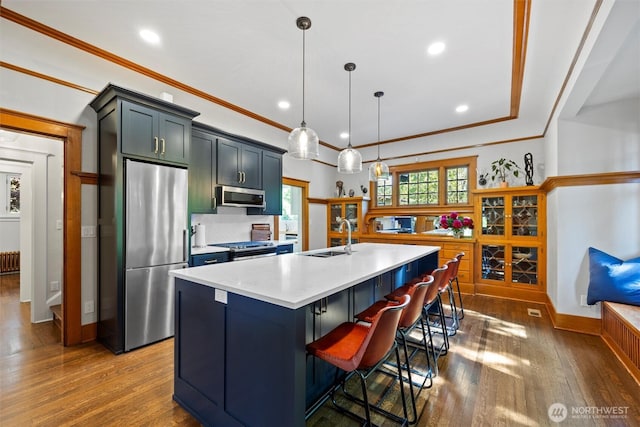 kitchen with stainless steel appliances, a sink, dark wood finished floors, light countertops, and ornamental molding