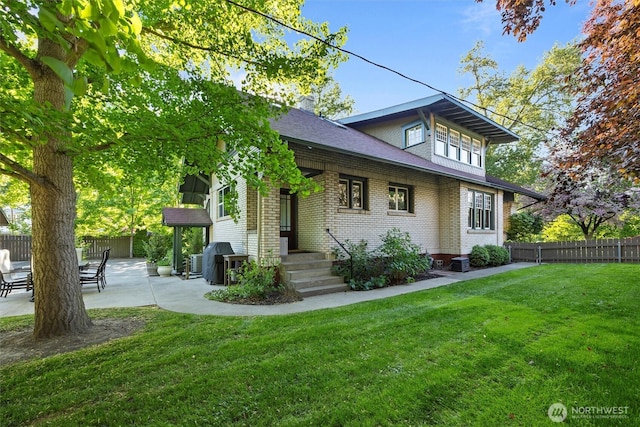 view of front facade featuring brick siding, a patio, a shingled roof, and a chimney