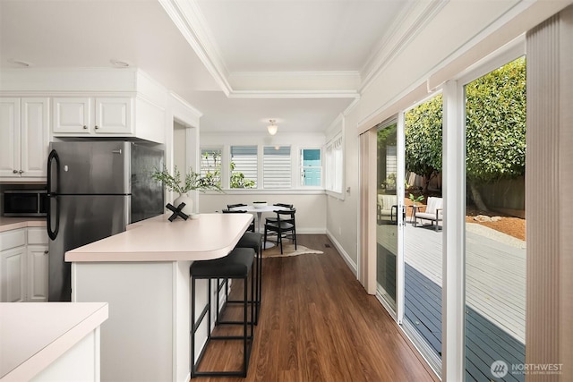 kitchen featuring freestanding refrigerator, white cabinetry, dark wood-type flooring, crown molding, and a kitchen bar