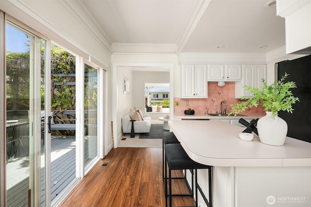 kitchen featuring light countertops, crown molding, a sink, white cabinets, and wood finished floors