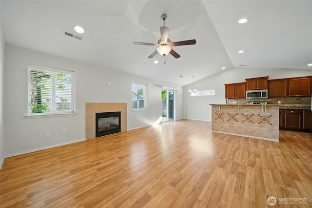 unfurnished living room featuring lofted ceiling, light wood-style floors, a tiled fireplace, ceiling fan, and recessed lighting