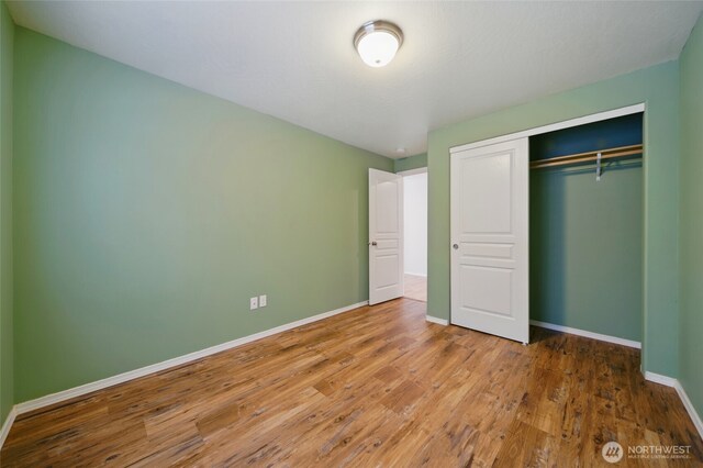 unfurnished bedroom with baseboards, wood finished floors, and a closet
