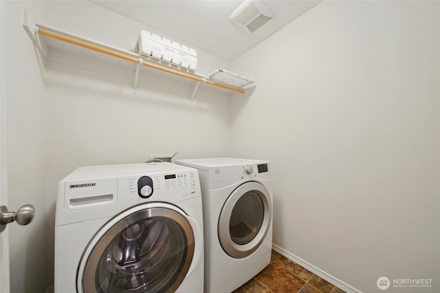 clothes washing area with separate washer and dryer, baseboards, and dark stone finish floors