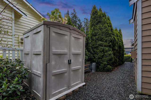 outdoor structure at dusk with a storage unit, an outbuilding, and fence