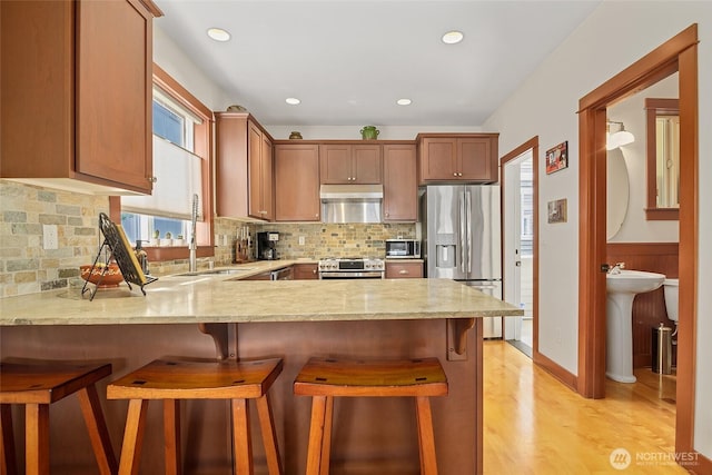 kitchen featuring appliances with stainless steel finishes, a sink, under cabinet range hood, a peninsula, and light wood-style floors