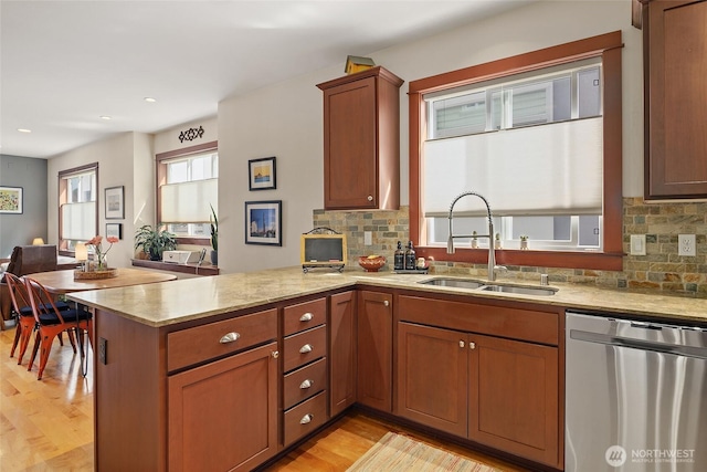 kitchen with dishwasher, a sink, a peninsula, light wood-style floors, and tasteful backsplash