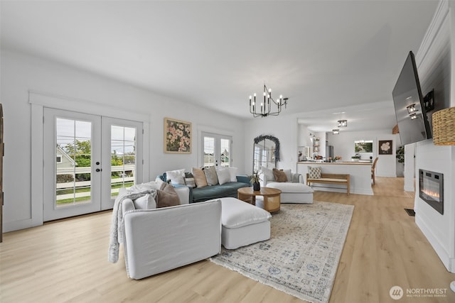 living area featuring light wood-type flooring, a chandelier, french doors, and a glass covered fireplace