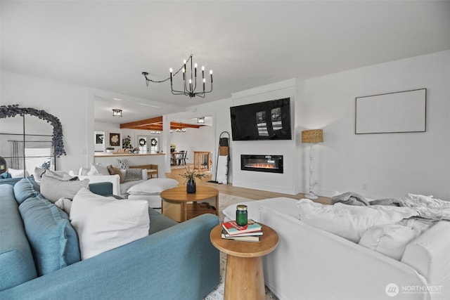 living area with a chandelier, light wood-type flooring, and a glass covered fireplace