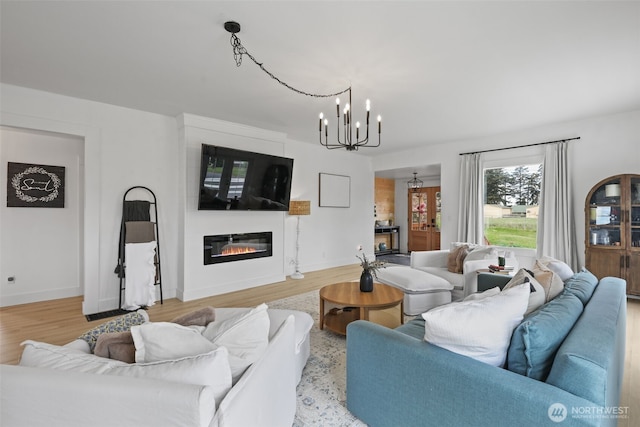 living area featuring a chandelier, a glass covered fireplace, light wood-type flooring, and baseboards