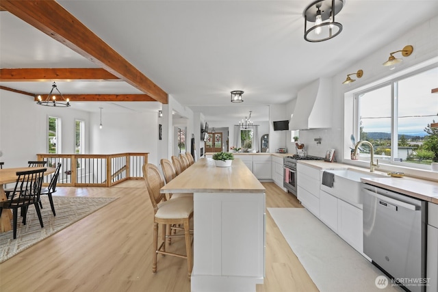 kitchen with appliances with stainless steel finishes, a chandelier, premium range hood, light wood-style flooring, and a breakfast bar area