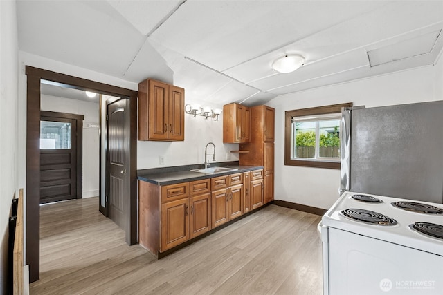 kitchen with freestanding refrigerator, electric range, a sink, brown cabinetry, and light wood-type flooring