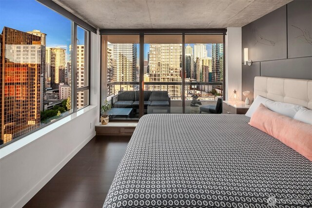 bedroom with a view of skyline, floor to ceiling windows, baseboards, wood finished floors, and access to outside