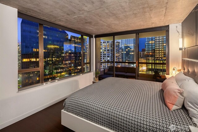 bedroom with a view of city, wood finished floors, and baseboards