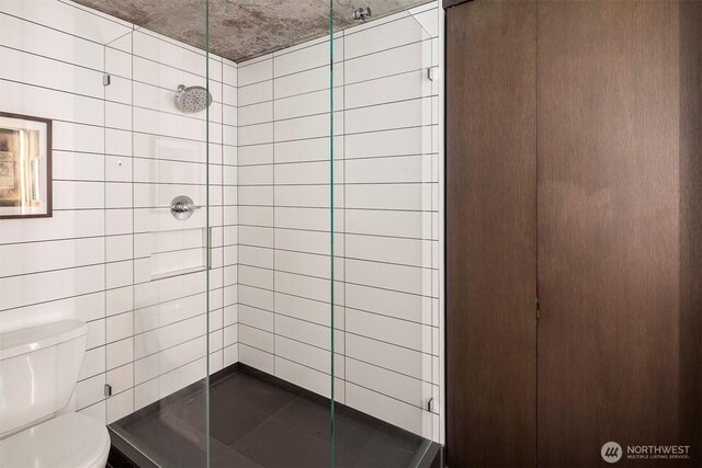 bathroom featuring a stall shower, toilet, and tile walls