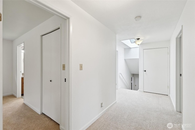 corridor featuring an upstairs landing, carpet flooring, a skylight, and baseboards