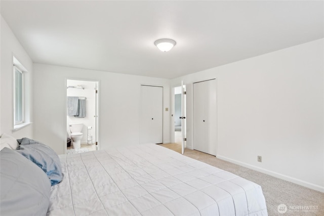 bedroom with light colored carpet, baseboards, connected bathroom, and two closets