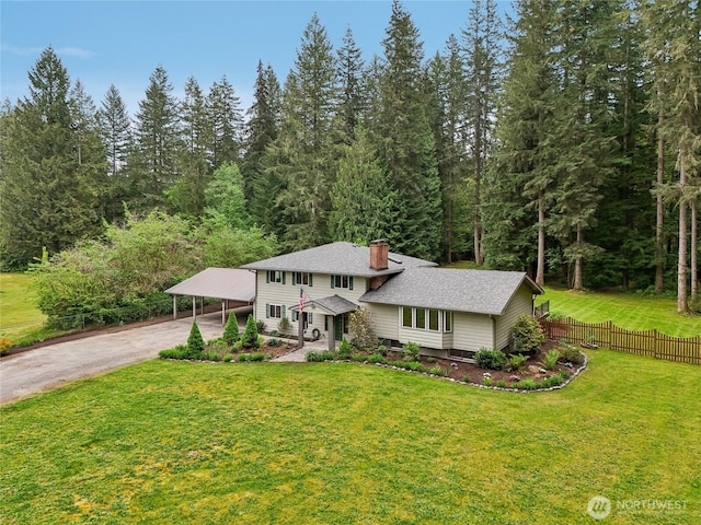 view of front of house with a chimney, a wooded view, a carport, and driveway
