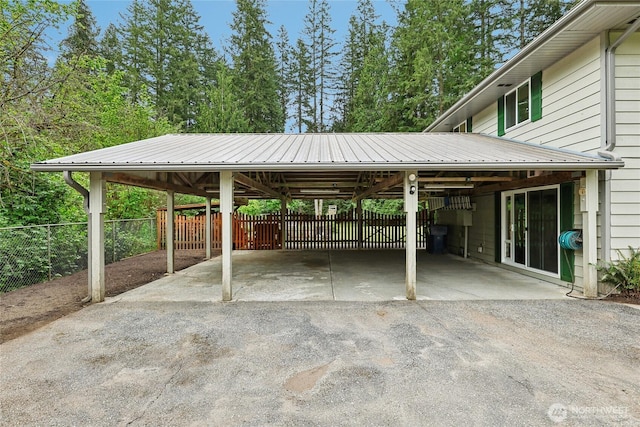 view of parking with asphalt driveway, fence, and an attached carport
