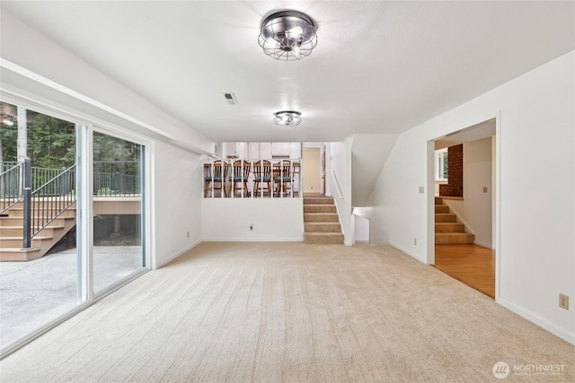 unfurnished living room featuring stairs, carpet floors, and baseboards