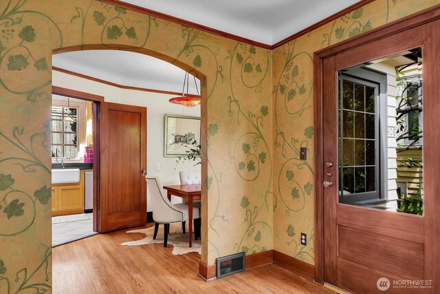 entrance foyer featuring light wood-type flooring, ornamental molding, arched walkways, wallpapered walls, and baseboards