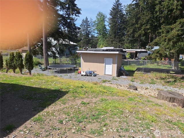 view of yard featuring a trampoline, a storage unit, fence, and an outbuilding