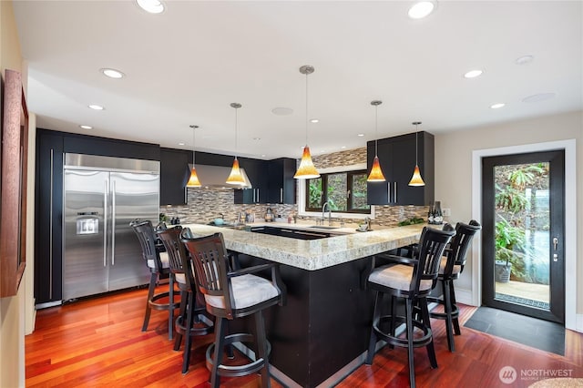 kitchen with built in refrigerator, tasteful backsplash, a peninsula, a breakfast bar, and recessed lighting