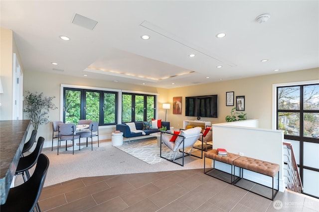 living room featuring recessed lighting, a tray ceiling, and baseboards