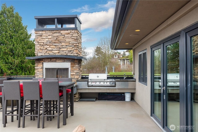 view of patio featuring grilling area, an outdoor stone fireplace, exterior kitchen, and a bar