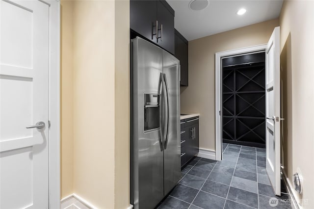 kitchen with stainless steel refrigerator with ice dispenser, dark cabinetry, light countertops, baseboards, and recessed lighting